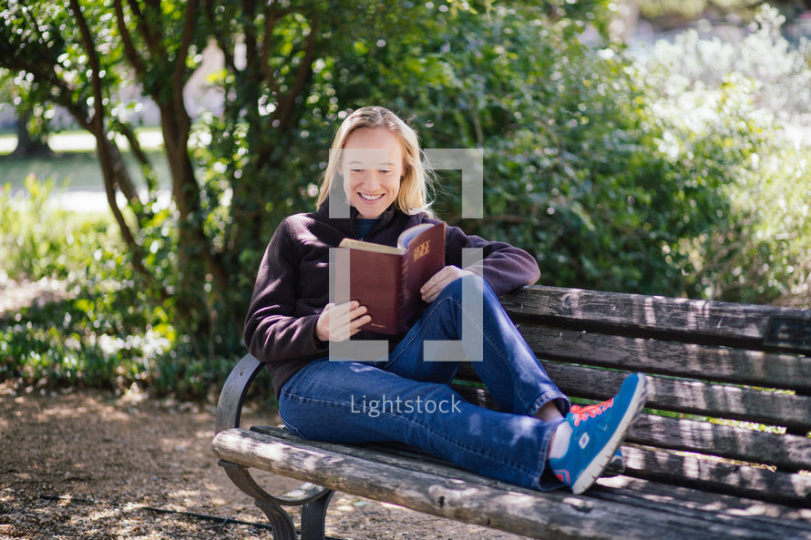 woman reading a Bible while sitting on a park bench