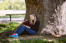 young woman sitting under a tree reading a Bible