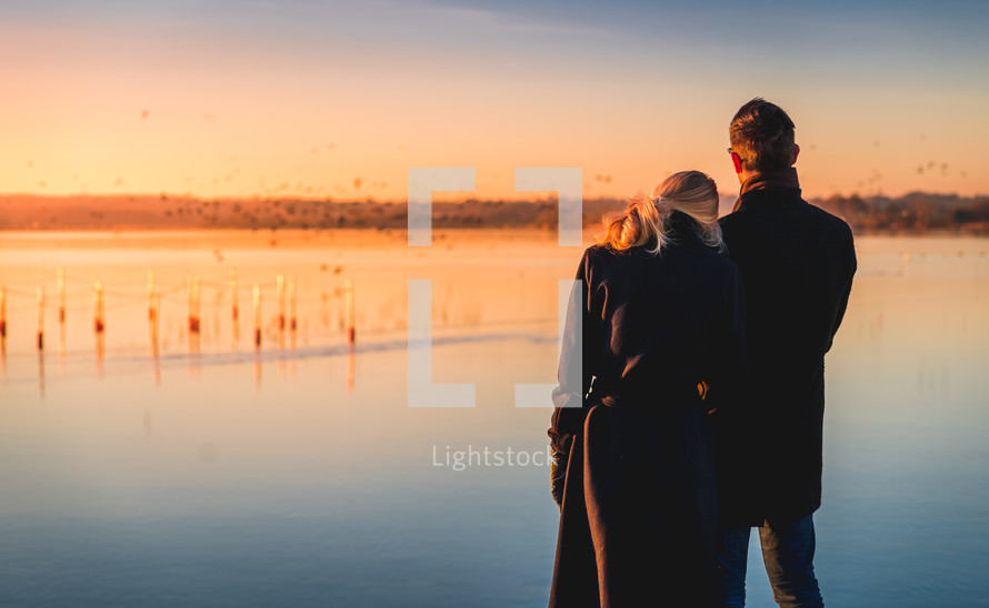a couple standing on a shore snuggling at sunset 