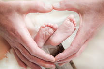 Infant feet surrounded by a father's hands.
