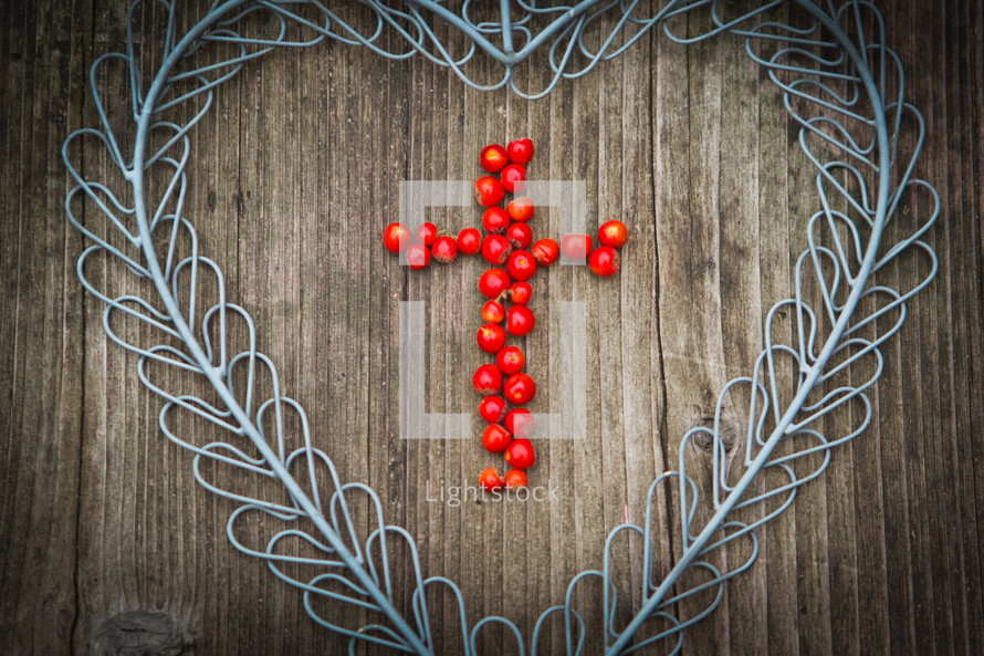 cross of berries in a blue metal heart on a wood background 