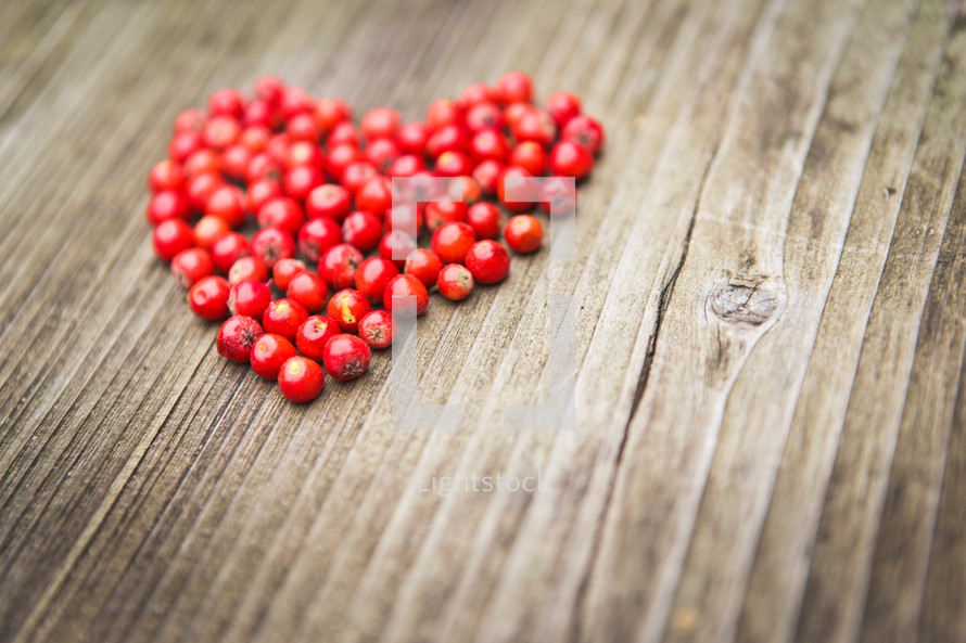 a heart of red berries on a wood background 