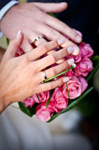 Bride and groom's hands together on a flower bouquet.