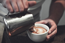 Hands pouring cream into coffee.