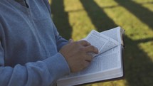 a man standing outdoors reading a Bible 