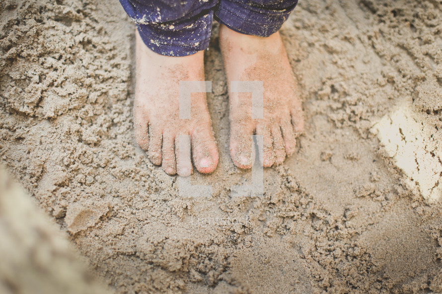 a child with feet in the sand box 