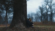 a woman sitting under a tree praying 