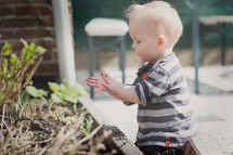 a toddler boy playing in dirt from a flower bed 