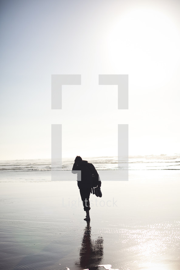 Silhouette of person walking on the beach at dusk.