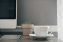 a cup and saucer on a desk in front of a computer screen 