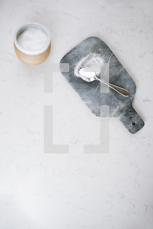 spoon of sugar and bowl on a cutting board in a kitchen 