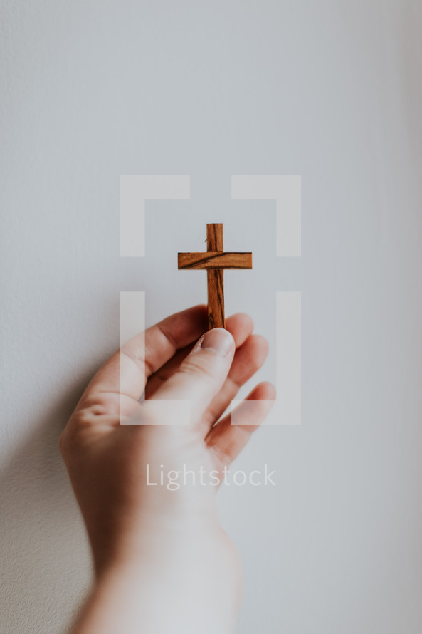 Hand with small wooden cross on white background