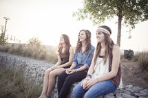 three young women sitting on a stone wall 