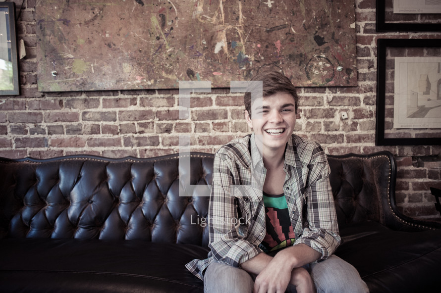 young man sitting on a leather couch smiling 