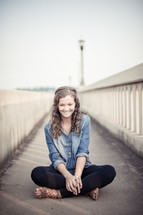 Smiling girl sitting on a bridge with rails.