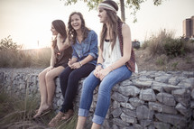 young women sitting on a stone wall together 