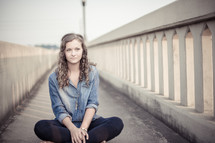 teen girl sitting on a sidewalk 