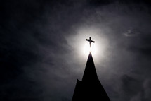 light shining on a cross on a steeple 