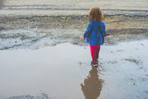 a toddler girl walking through a puddle 