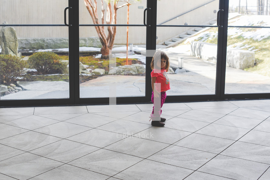 a toddler girl standing in front of glass doors 
