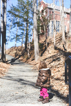 a toddler girl in a coat on a gravel path 
