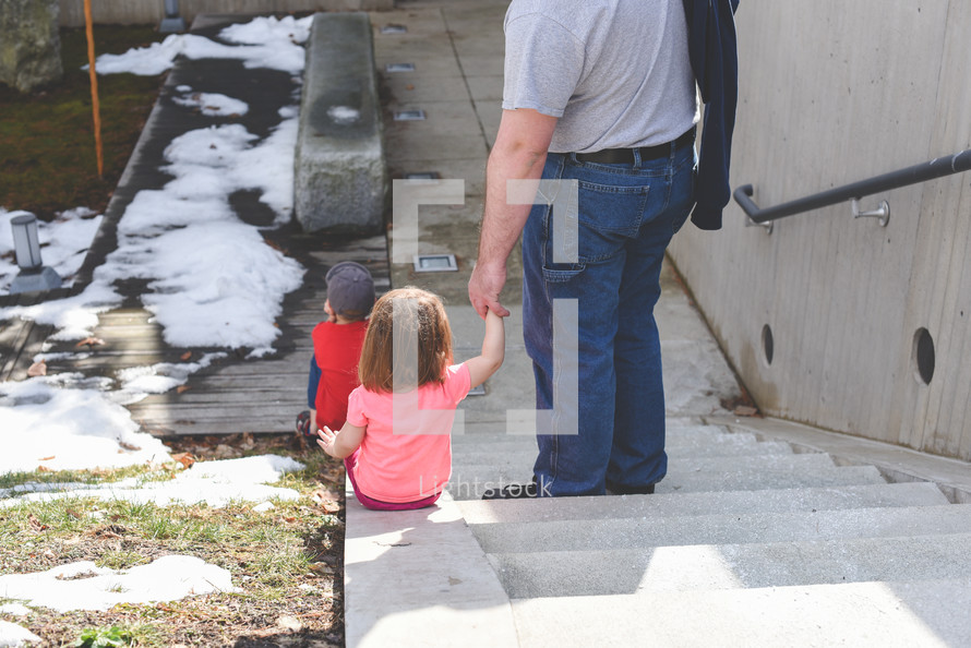 a father holding his daughters hand on steps 