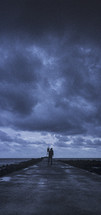 man standing on a jetty under a cloudy sky 