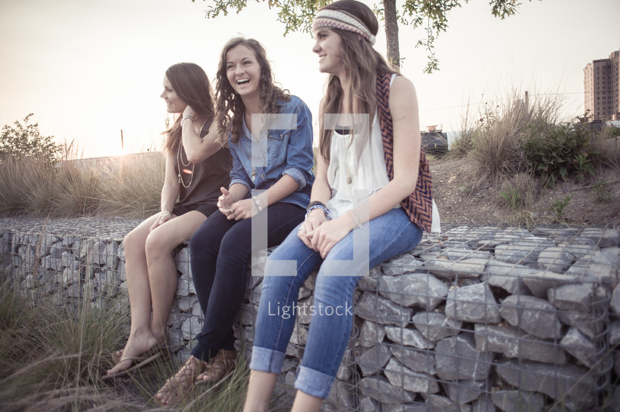 young women sitting on a stone wall together 