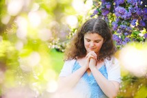 a girl in a dress praying under a flowering tree 