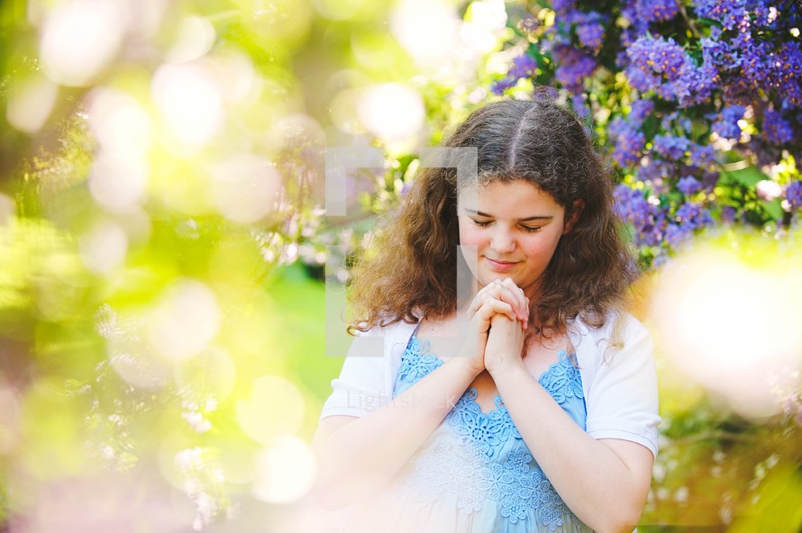 a girl in a dress praying under a flowering tree 