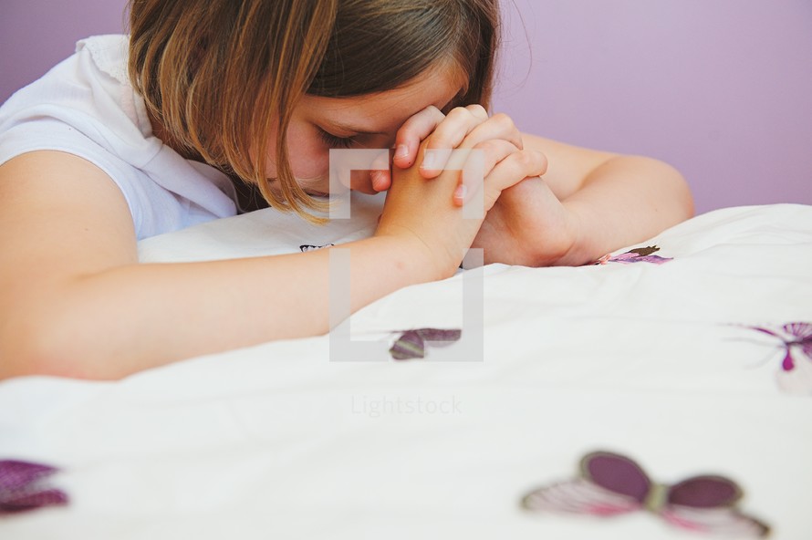 a girl kneeling in prayer by her bedside 
