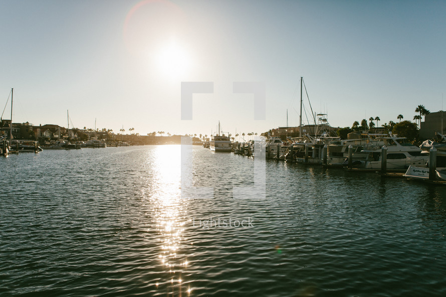 Boats docked in a harbor with the reflection of the sun on the water.