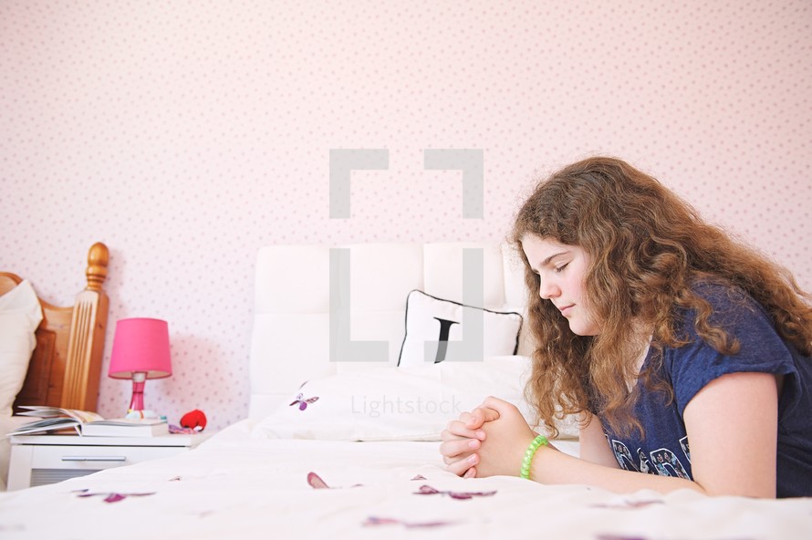 a girl kneeling in prayer beside her bed 