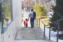 a father holding hands with his daughter walking down steps 