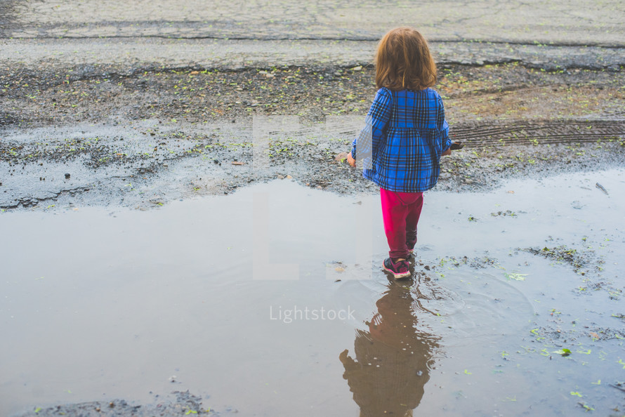 a toddler girl walking through a puddle 