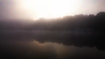 lake fly over with drone on misty fog covered lake morning sun rising above the pine tree forest