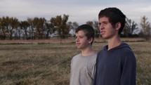 Two happy, smiling young men, best friends, standing in nature watching the summer sunset in cinematic slow motion. 