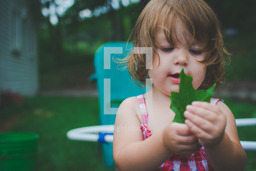 a toddler girl holding a green leaf 