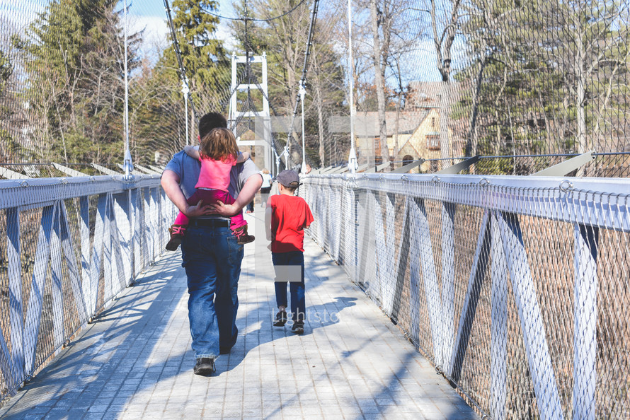 a father walking across a swinging bridge with his kids 