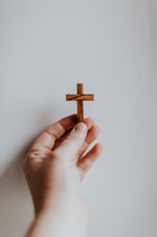 Hand with small wooden cross on white background