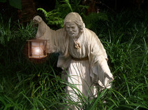Statue of an Israelite holding a lantern to light his way through a thick path of grass and weeds as he travels by night.