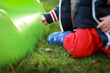 a toddler boy sitting in grass on a playground 