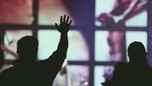 raised hands at a worship service with projection screen of the crucifixion 