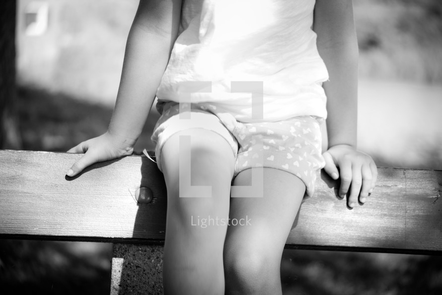 a girl child sitting on a park bench 