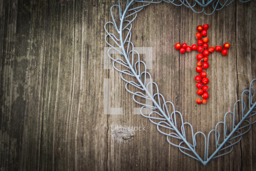a cross of red berries in a blue metal heart on a wood background 
