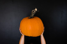 hands holding up a pumpkin against a black background 