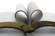Spine of Bible with gold-edge inside pages folded in to make a heart shape, lying on table