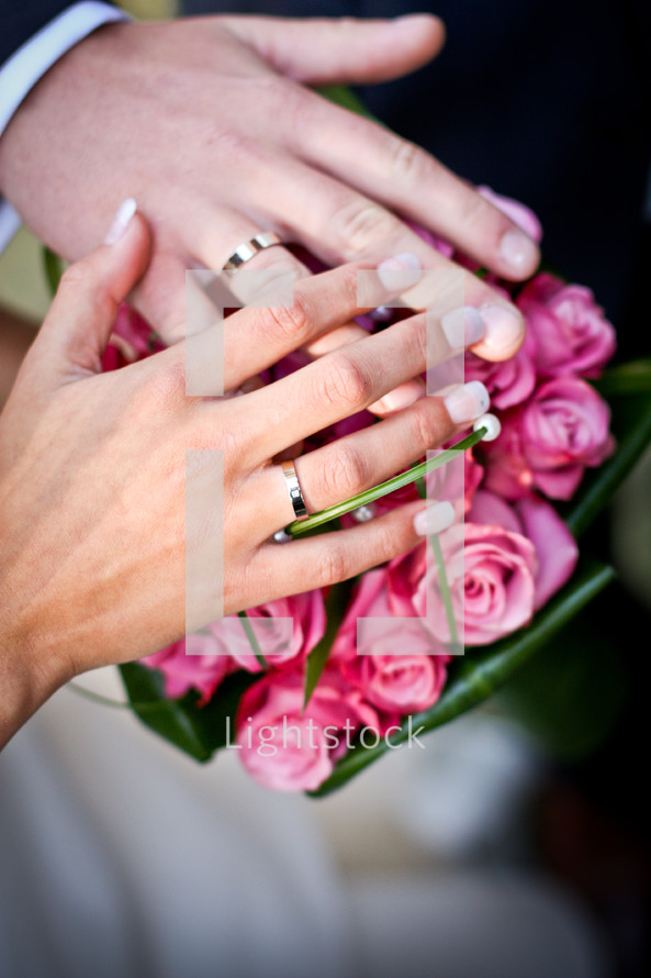 Bride and groom's hands together on a flower bouquet.