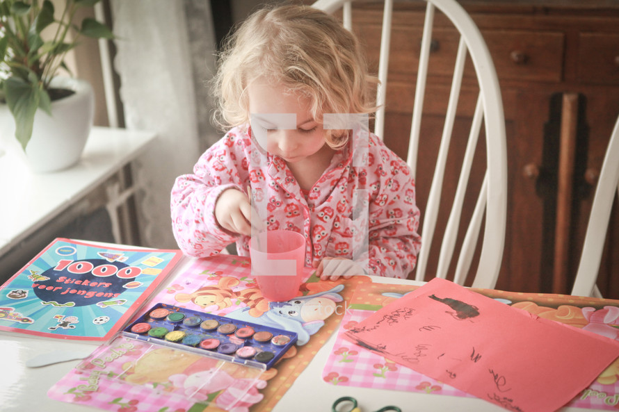 A little girl water coloring at the kitchen table.