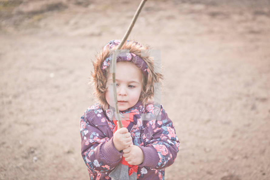 a child in a winter coat holding a stick 